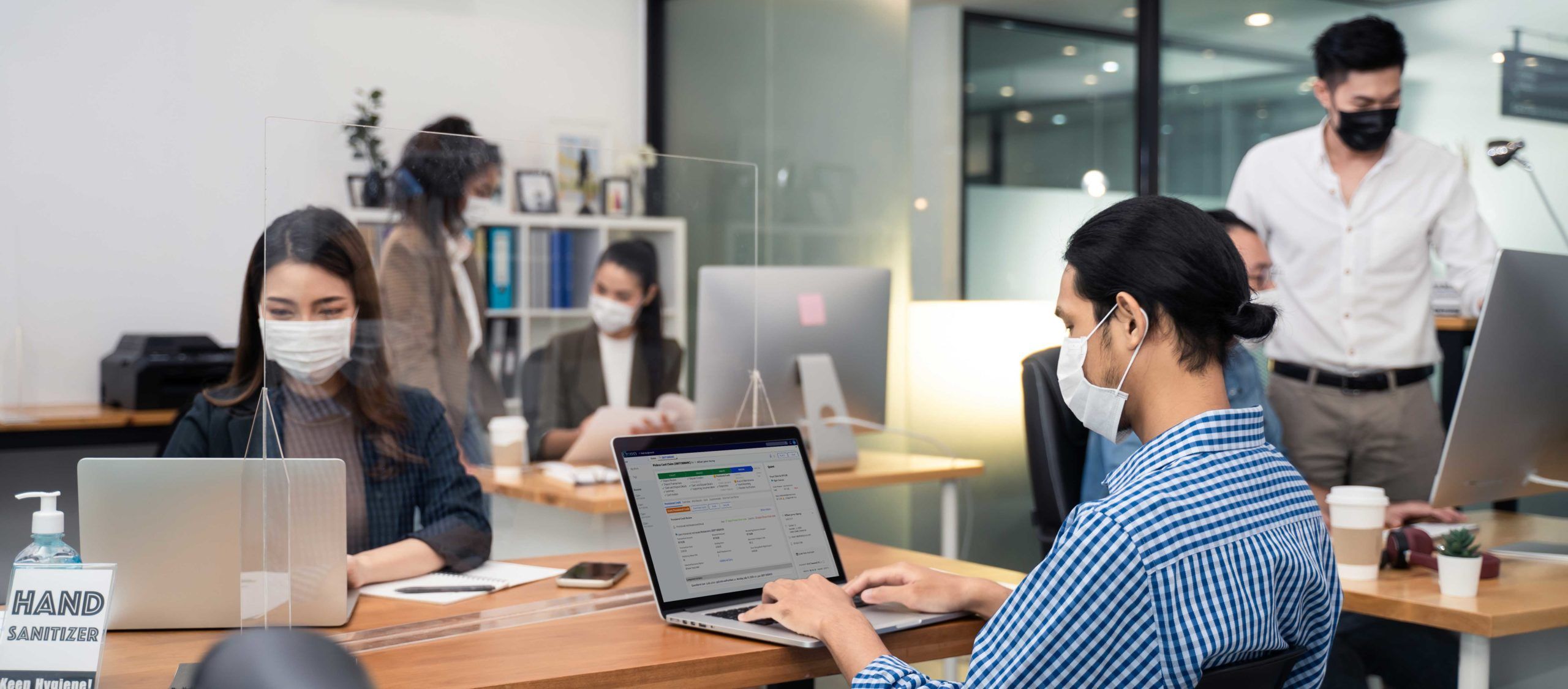 Man and woman sitting in office with face masks, man working on computer with QFD software